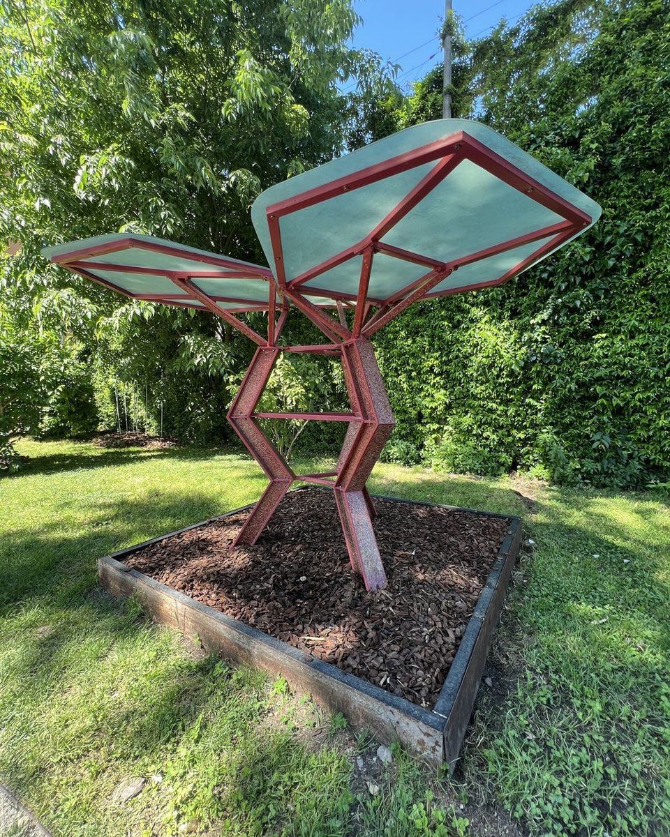 A red steel frame holding two curved translucent panels in a planted garden bed.