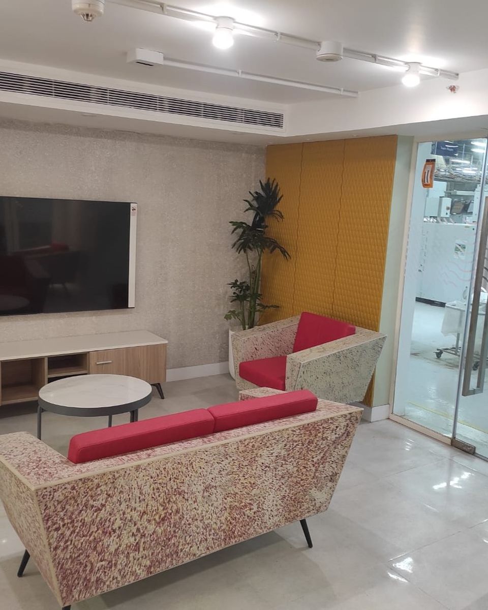 A sofa and armchair with red cushions on speckled frames, with a coffee table in an office lounge.