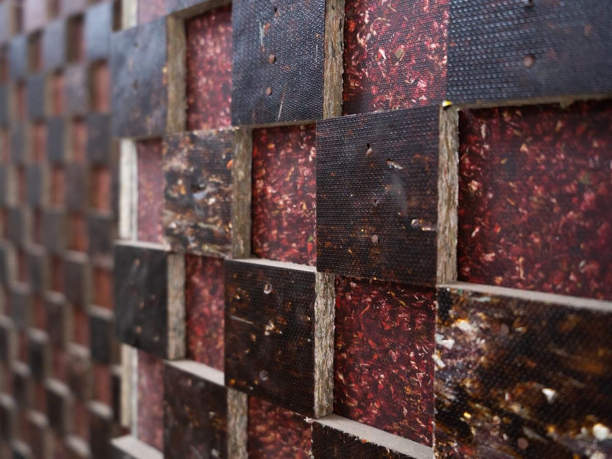 A wall of alternating square panels, one set dark and studded, one set deep red with a speckled recycled texture.