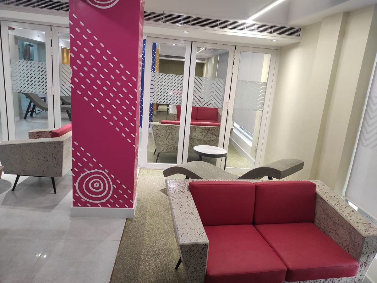 A lounge with red-upholstered seating on speckled composite frames, beside a painted patterned column.