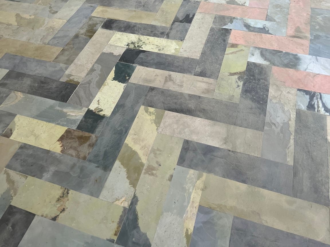 Multicoloured herringbone flooring in grey, cream, pink and olive strips, viewed from above.