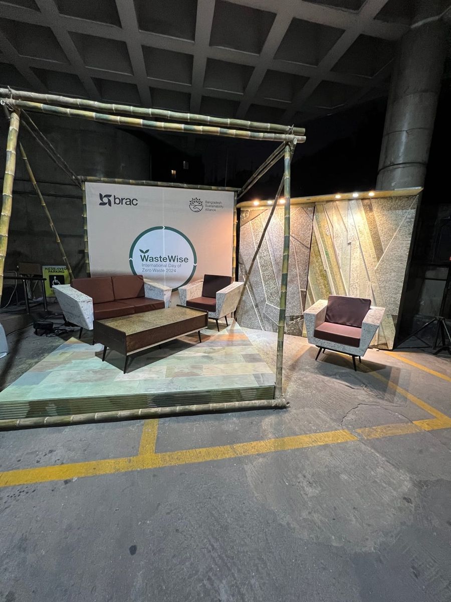 A full exhibition display with a sofa, two armchairs, a coffee table and patterned panels in front of a WasteWise 2024 banner.