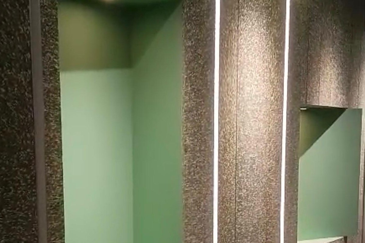 A corridor feature wall of gold-toned composite panels with lit green display niches and vertical light strips.